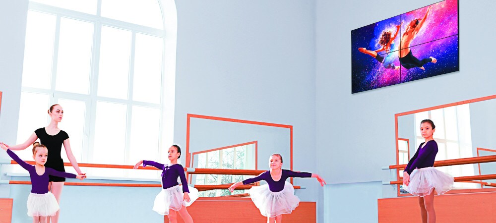 Digital signage display on the wall. Kids learning to dance ballet in a room